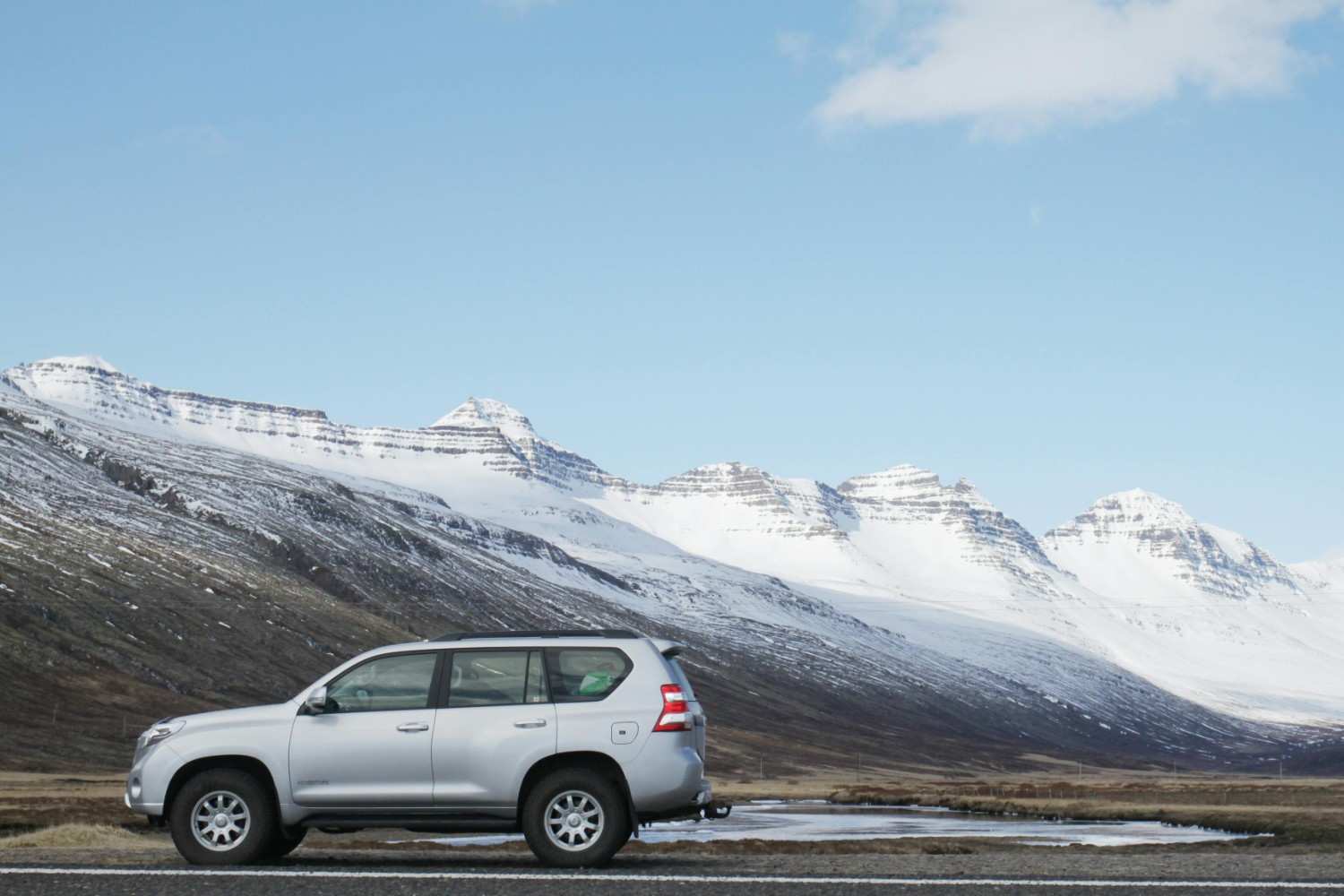 A modern silver SUV driving on a clean open highway through a scenic mountain range